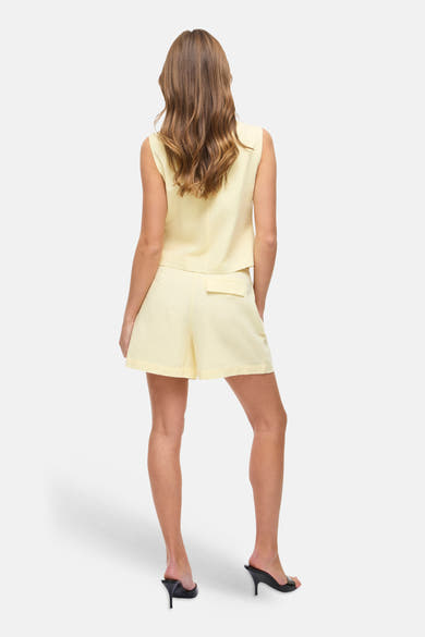 Gele korte broek van VILA, met een rechte pasvorm en een opgestikte zak aan de achterkant, gedragen met zwarte naaldhakken.