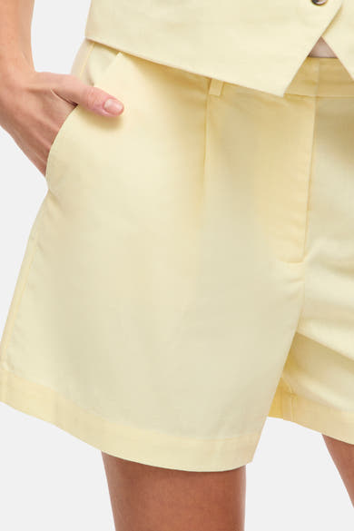 Korte gele broek van VILA, met één hand in de zak en onderdeel van een gecoördineerde set.