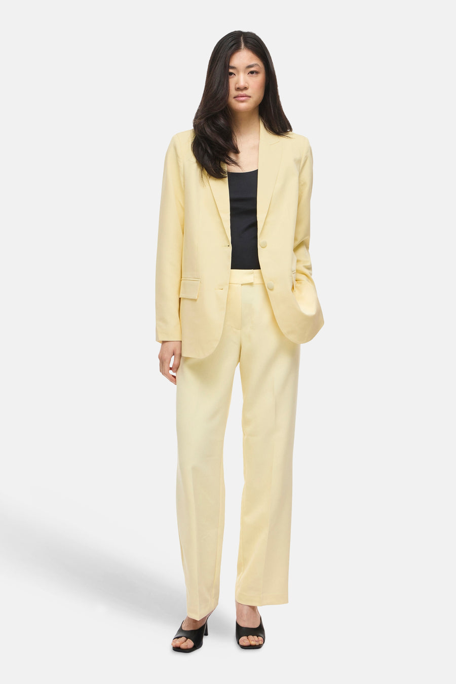 Blazer jaune par VILA®, porté avec un débardeur noir et un pantalon assorti, chaussures noires à talons.