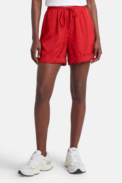 Korte rode rok van VILA®, elastische tailleband met trekkoord en omgeslagen zomen, gedragen met een wit T-shirt en sneakers.