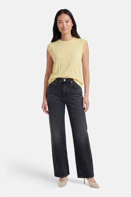 Gele mouwloze top van VILA® met kanten rand, gedragen met een zwarte jeans en hakken.