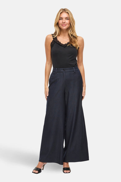 Pantalon ample bleu de VILA, porté avec un haut noir à dentelle et des chaussures à talons ouvertes.