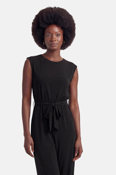 Combinaison noire de VILA® sans manches avec ceinture à nouer, portée par un mannequin aux cheveux afro et boucles d'oreilles créoles.