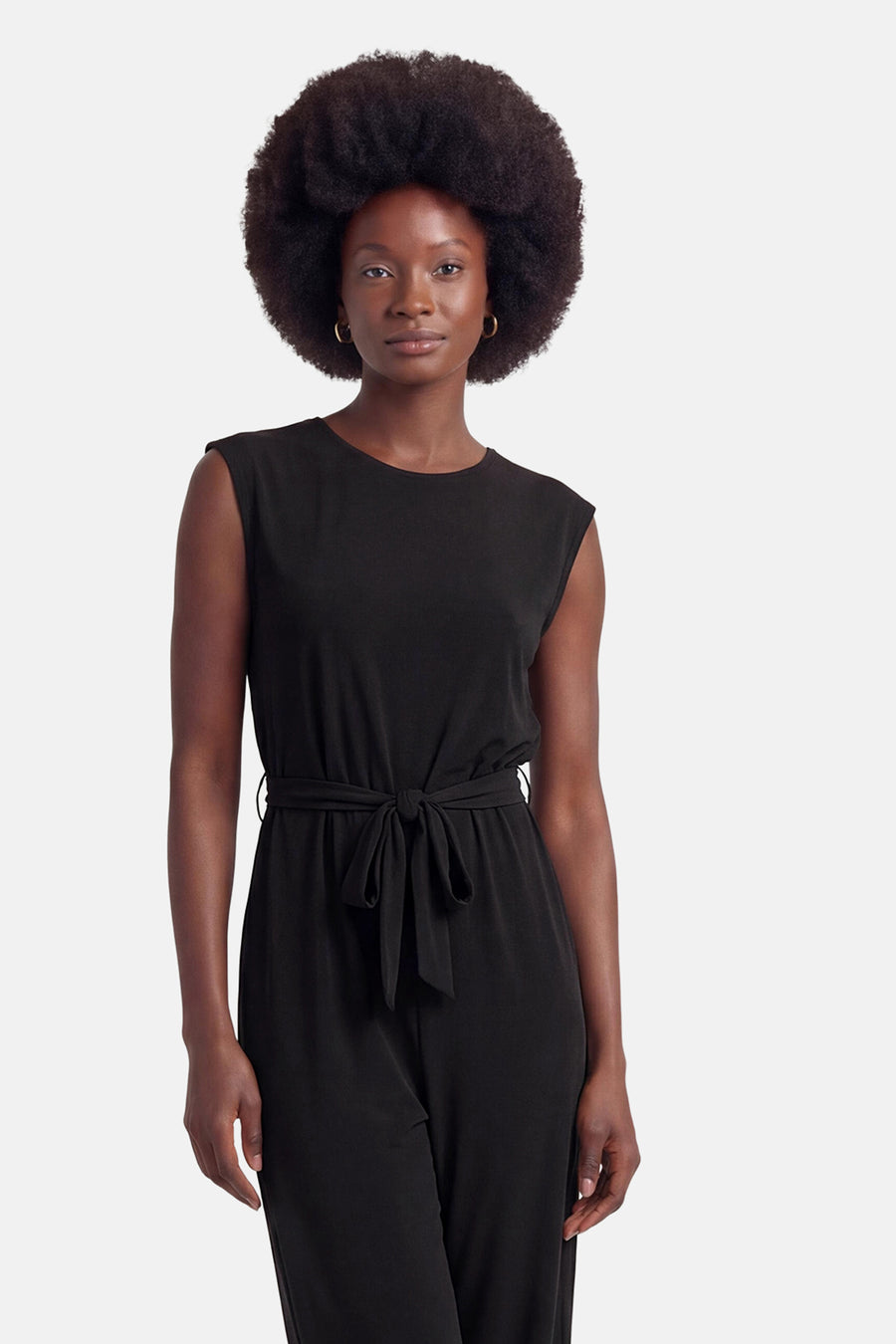 Combinaison noire de VILA® sans manches avec ceinture à nouer, portée par un mannequin aux cheveux afro et boucles d'oreilles créoles.