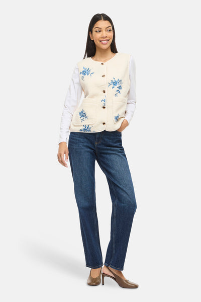 Veste sans manches beige de VILA®, à boutons et broderie florale bleue, portée sur un haut blanc et un jean.
