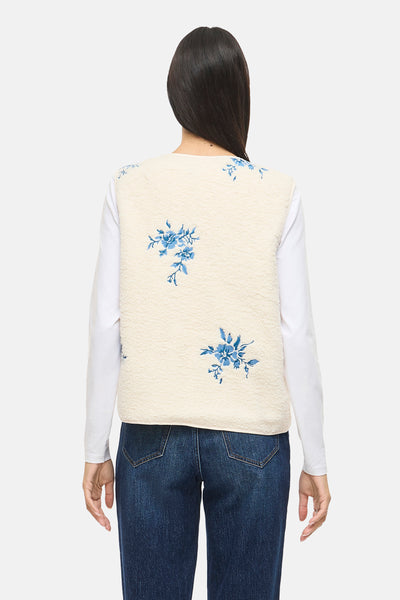 Beige mouwloos vest van VILA, met blauw bloemenpatroon, gedragen over een witte top en een donkerblauwe jeans.