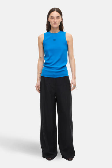 Top bleu sans manches de ROUGE EDIT, porté avec un pantalon noir ample.
