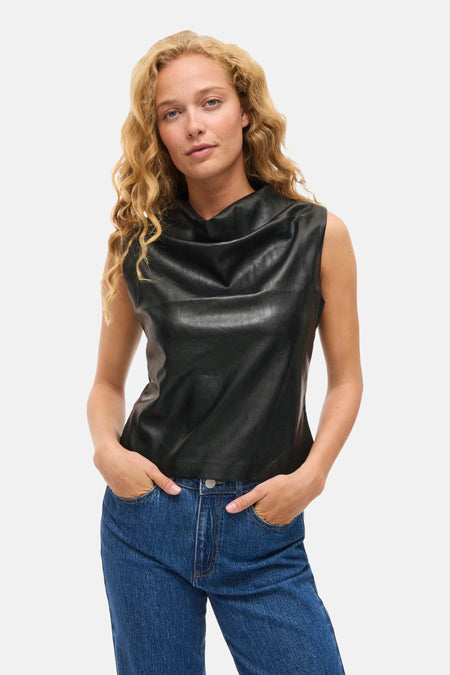 Zwart mouwloos hemd van VILA, gedragen met een blauwe jeans en handen in de zakken.