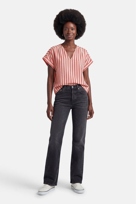 Blouse à rayures verticales rouges et crème de VILA®, col en V et manches courtes, portée avec un jean noir et des baskets blanches.