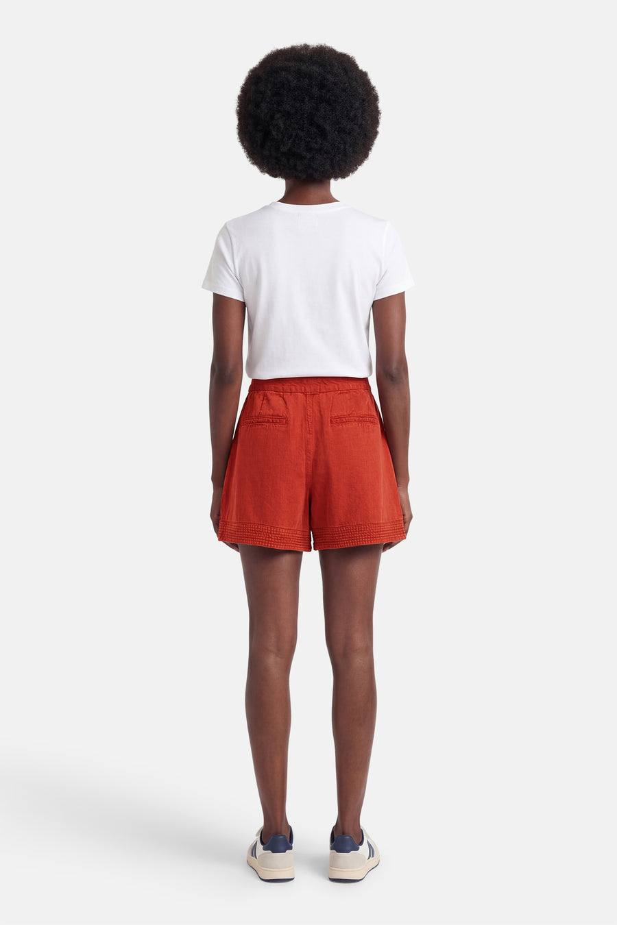 Korte oranje short van VILA®, in getextureerde stof met een decoratieve band aan de zoom, van achteren gedragen met een wit T-shirt en lichte sneakers.