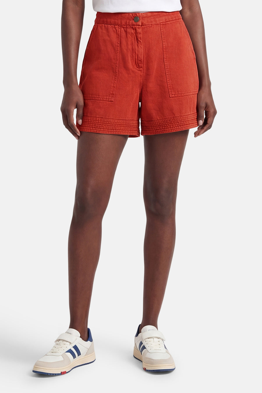 Korte oranje short van VILA® met opgestikte zakken en elastische zomen, gedragen door een vrouw met sneakers.
