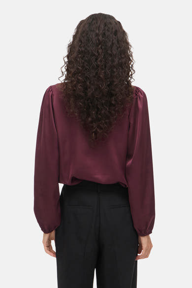 Bordeaux blouse met lange mouwen van VILA, met krullend haar en een zwarte broek.