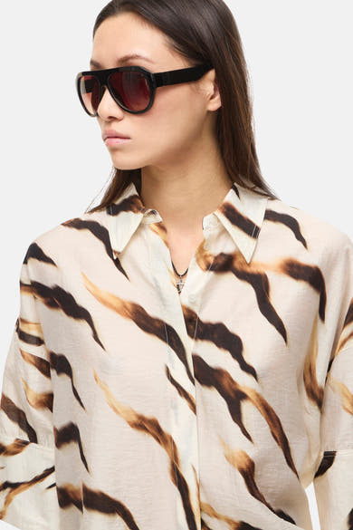 Chemisier multicolore de ROUGE EDIT à imprimé animalier abstrait marron et beige, porté par une femme avec des lunettes de soleil noires et un collier.