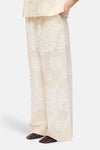 Pantalon large beige de ROUGE EDIT avec broderie florale blanche, porté avec des mocassins marron.