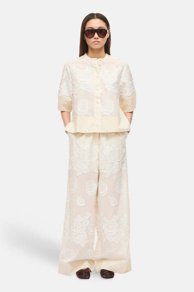 Pantalon beige de ROUGE EDIT avec motif floral en dentelle blanche et coupe ample, porté avec un haut assorti.