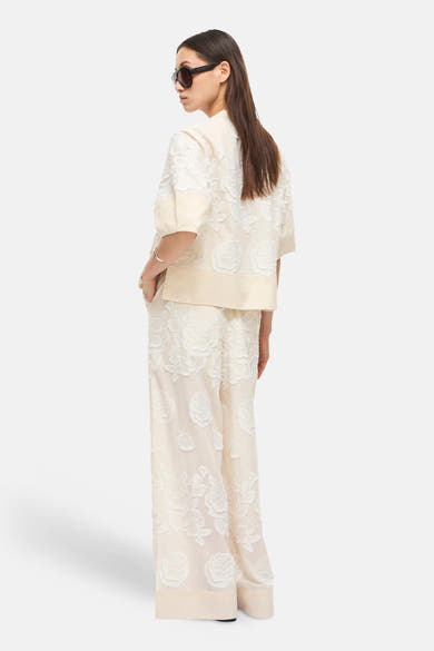 Pantalon beige de ROUGE EDIT à motifs floraux blancs brodés, coupe large, porté avec un haut assorti.