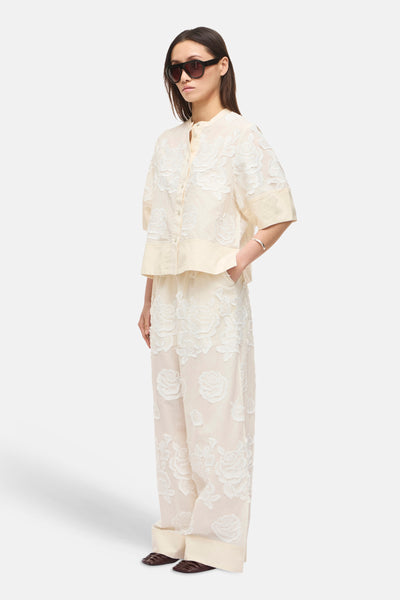 Blouse à manches courtes beige de ROUGE EDIT avec motif floral en dentelle, col mao et boutons, portée avec un pantalon assorti.