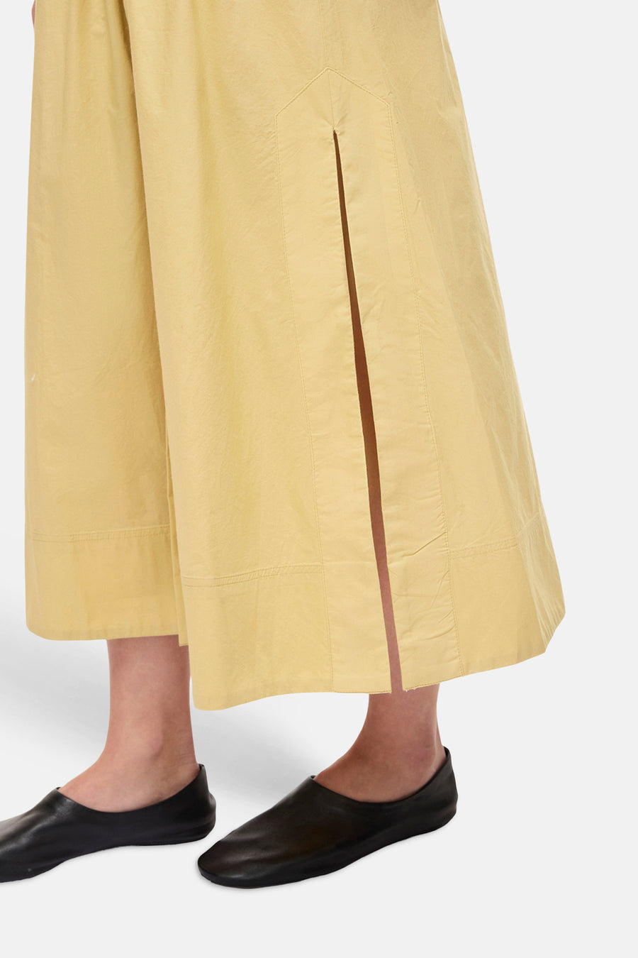 Robe jaune ample de ROUGE EDIT, à fente frontale avec surpiqûres, en tissu texturé, portée avec des mules noires.