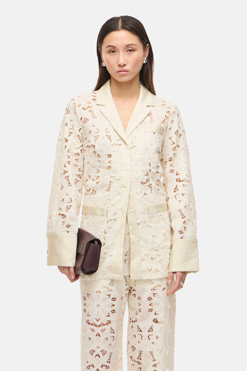 Blazer beige à motif ajouré de ROUGE EDIT, porté avec un pantalon coordonné et une pochette marron.
