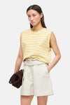Top rayé jaune et écru de ROUGE EDIT, sans manches, porté avec un short crème et un sac en daim marron.
