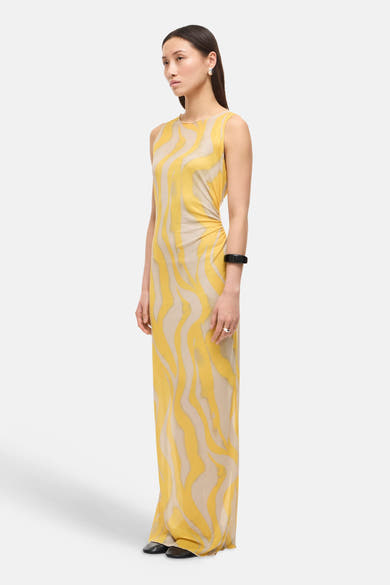 Multikleurenjurk van ROUGE EDIT, met geel en beige golvend patroon, zwart accessoire om de pols en zilveren ring.