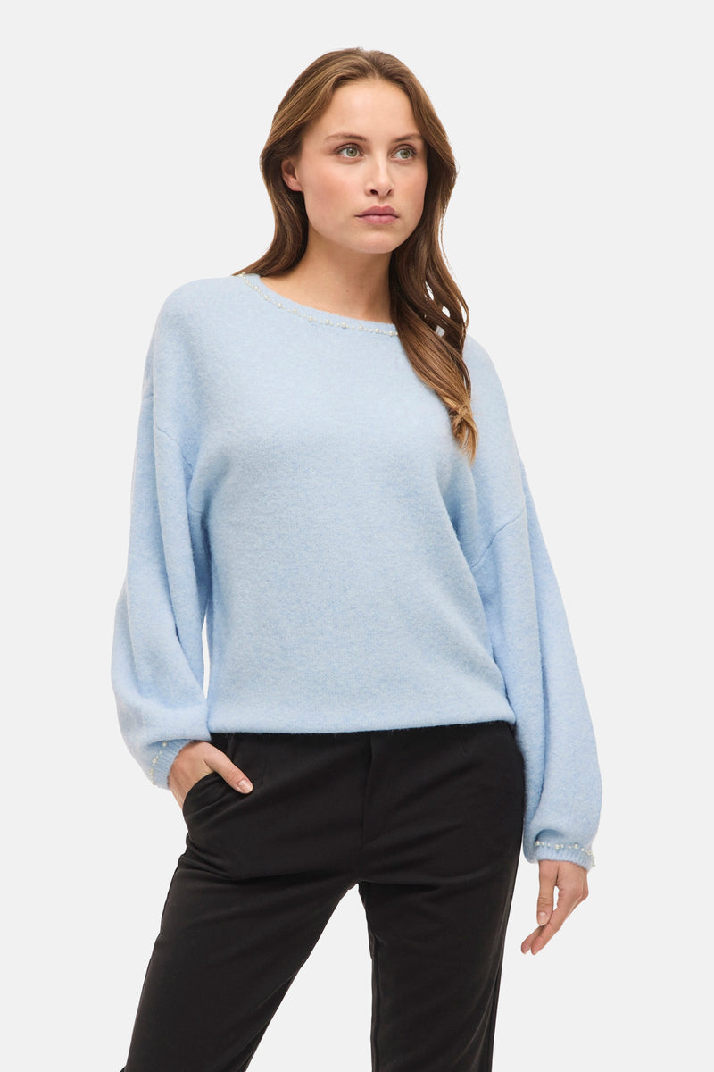 Ronde hals trui van VILA® in het blauw, versierd met discrete kralen, gedragen met een zwarte broek en zwarte pumps.