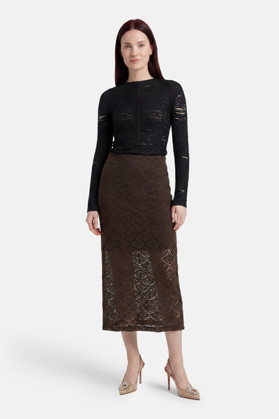 Brown lace long skirt with scalloped pattern, worn with black textured top and nude heels, front view