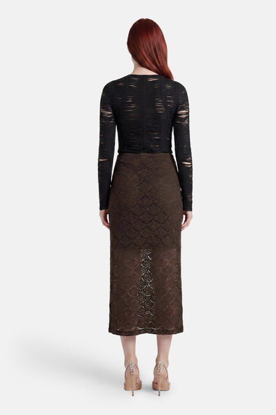 Brown lace long skirt with scalloped pattern, back view, worn with black sheer top and embellished heels