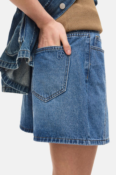 Short en jean bleu moyen de ROUGE EDIT avec logo brodé sur la poche arrière, porté avec une veste en jean et un haut tricoté marron.