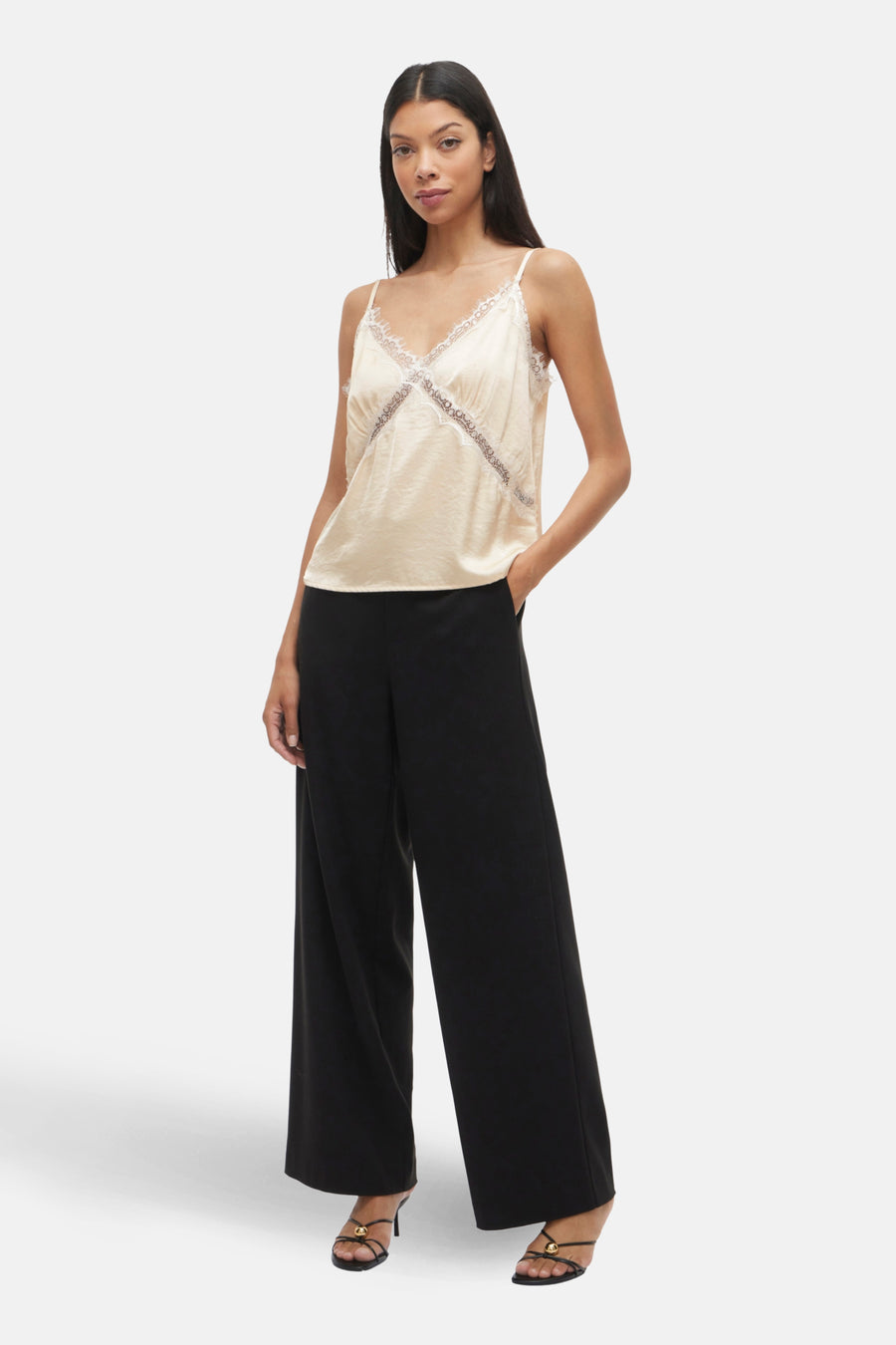 Blouse écru sans manches de VILA® ornée de dentelle, portée avec un pantalon noir large et des sandales à talons.
