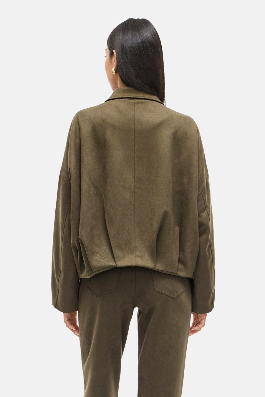 Korte groene suèdejas van VILA®, van achteren gezien, gedragen met een bijpassende broek en gouden oorbellen.