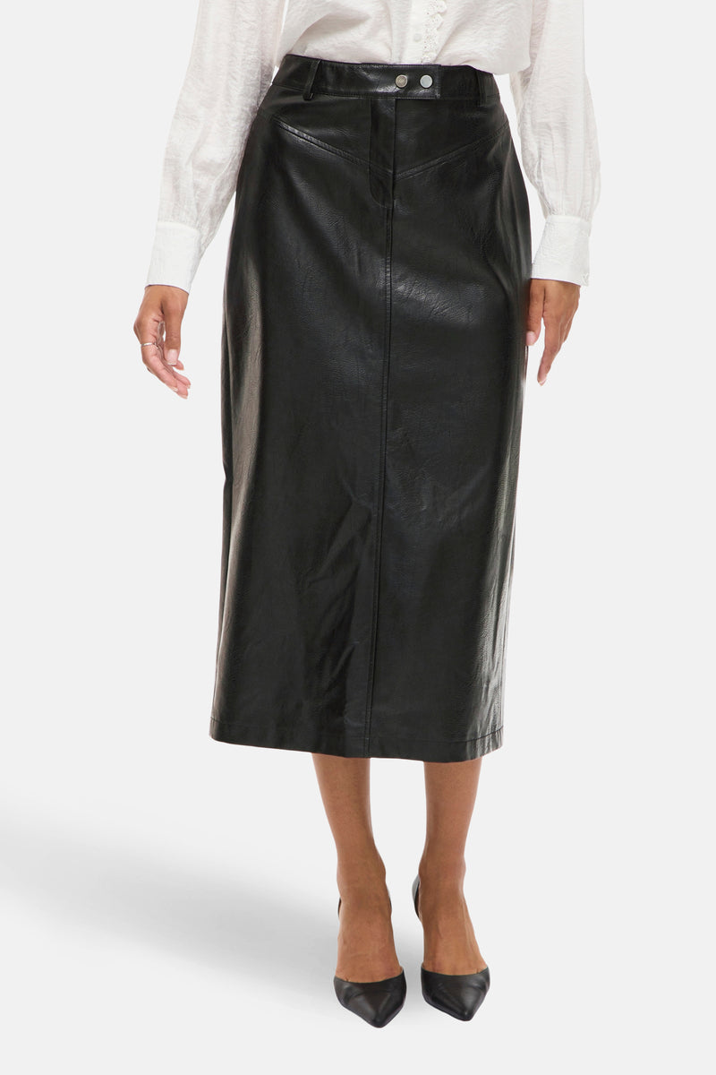 Jupe longue noire en similicuir par VILA®, avec une fente arrière, portée avec une chemise blanche.
