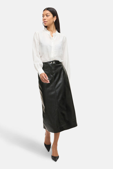 Jupe longue noire en simili cuir de VILA®, portée avec un chemisier blanc à jabot.