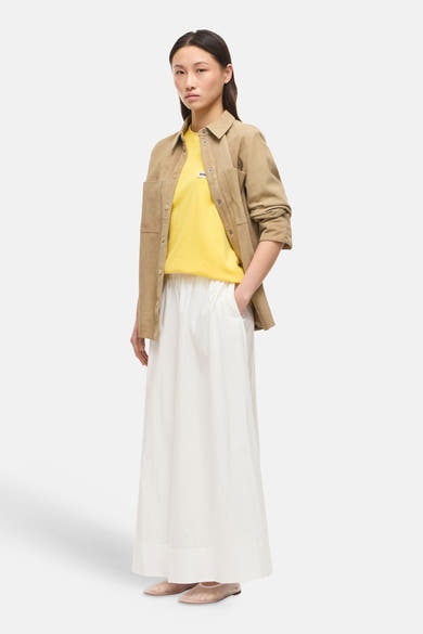 Jupe longue blanche de ROUGE EDIT, ample et fluide, portée avec un t-shirt jaune et une veste camel.
