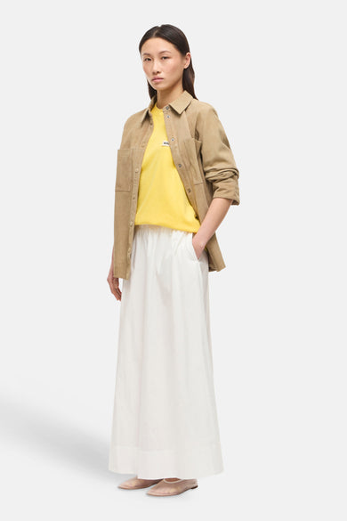 Jupe longue blanche de ROUGE EDIT, ample et fluide, portée avec un t-shirt jaune et une veste camel.
