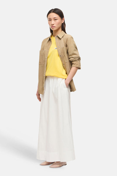 Jupe longue blanche de ROUGE EDIT, ample et fluide, portée avec un t-shirt jaune et une veste camel.
