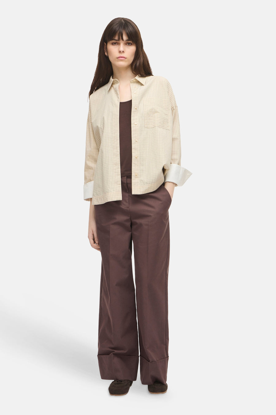 Beige long-sleeve shirt with fine check pattern, button-down front, and chest pocket, worn open over dark brown top and wide-leg trousers, full-length front view