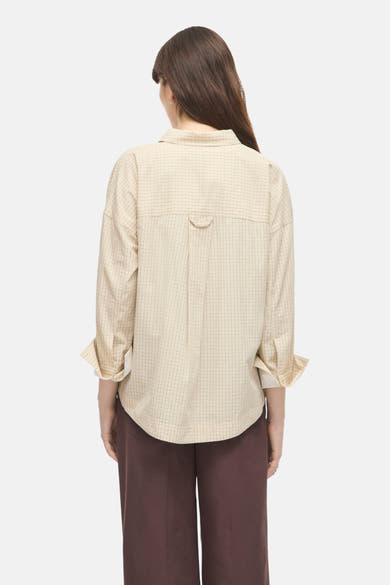 Beige long-sleeve checkered blouse with back pleat and cuffed sleeves, worn with brown trousers, back view