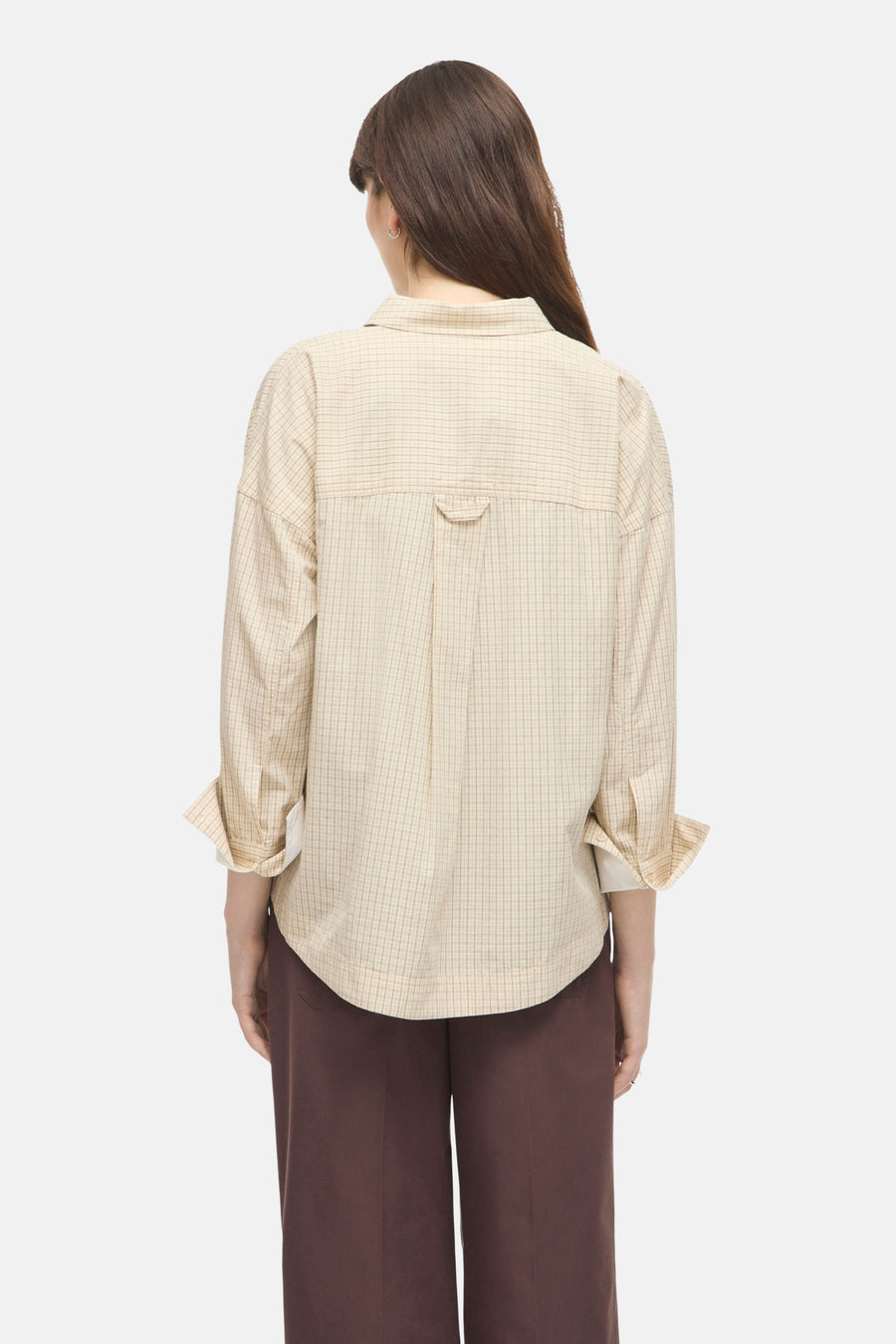 Beige long-sleeve checkered blouse with back pleat and cuffed sleeves, worn with brown trousers, back view