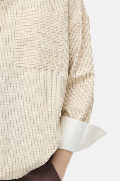 Beige long-sleeve blouse with fine check pattern and chest pocket, featuring rolled cuffs and white lining, side view close-up