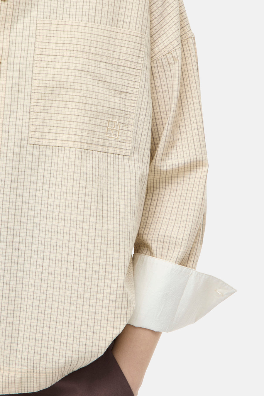 Beige long-sleeve blouse with fine check pattern and chest pocket, featuring rolled cuffs and white lining, side view close-up