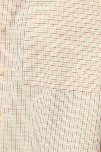 Beige long-sleeve blouse with fine check pattern and chest pocket featuring embroidered logo, close-up view