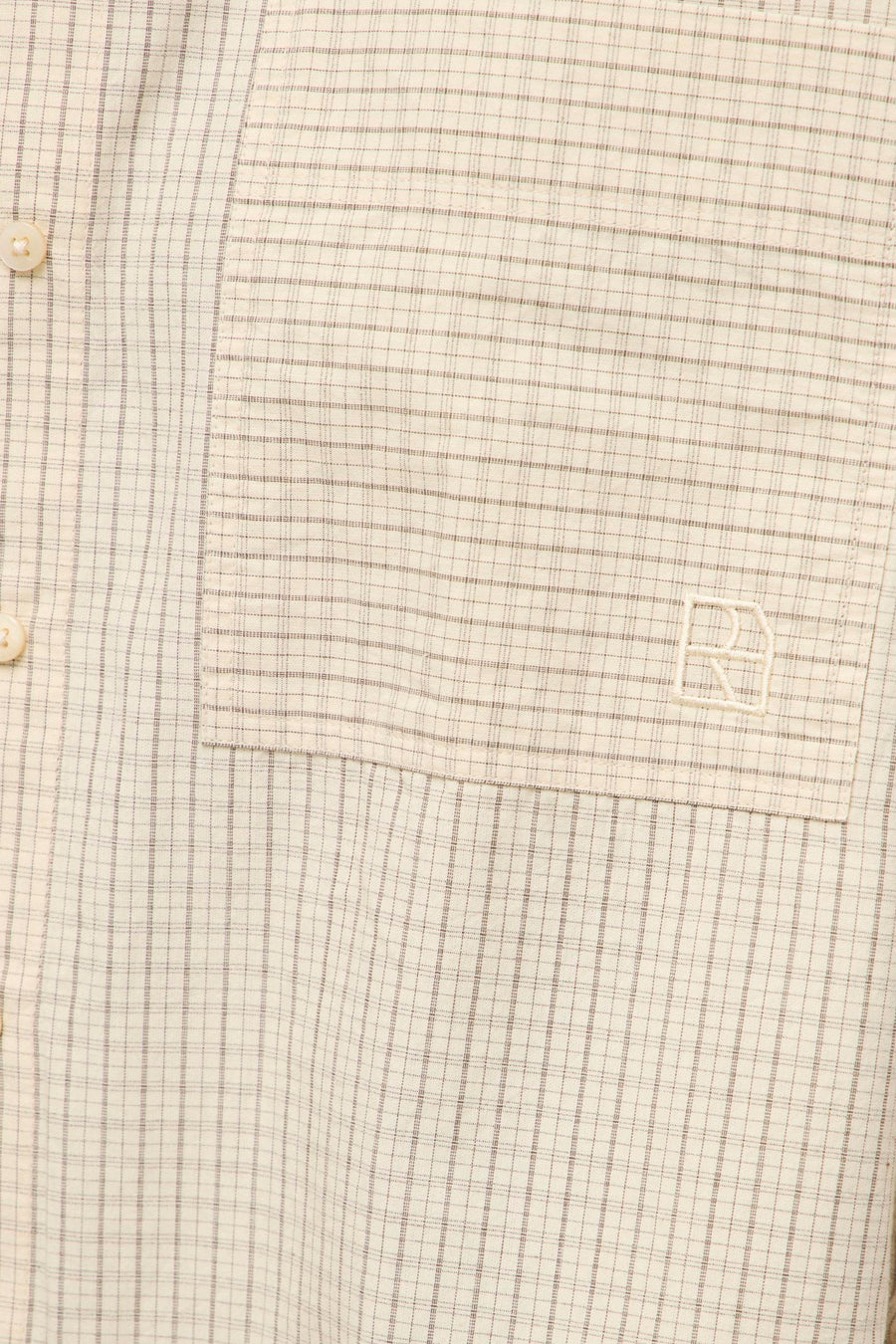 Beige long-sleeve blouse with fine check pattern and chest pocket featuring embroidered logo, close-up view