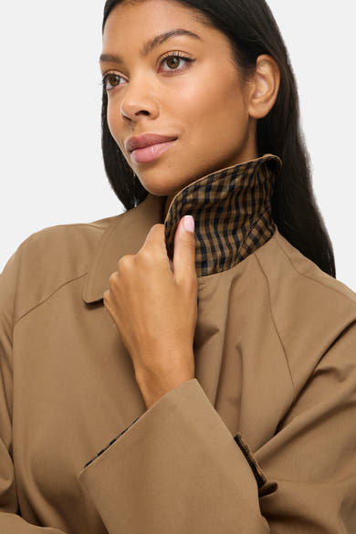 Femme portant un trench brun avec un col à carreaux brun et noir, vue rapprochée
