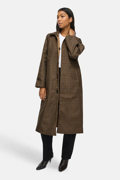 Manteau trench long brun à carreaux VILA® porté par un mannequin, avec jean noir et bottines.