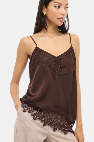 Débardeur marron en dentelle by VILA, avec fines bretelles et bordure en dentelle florale, porté avec un pantalon beige.
