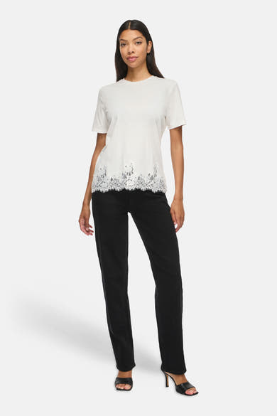 Top blanc uni à manches courtes avec bordure dentelle au bas, par VILA®, porté avec pantalon noir et sandales à talons, vue de face.