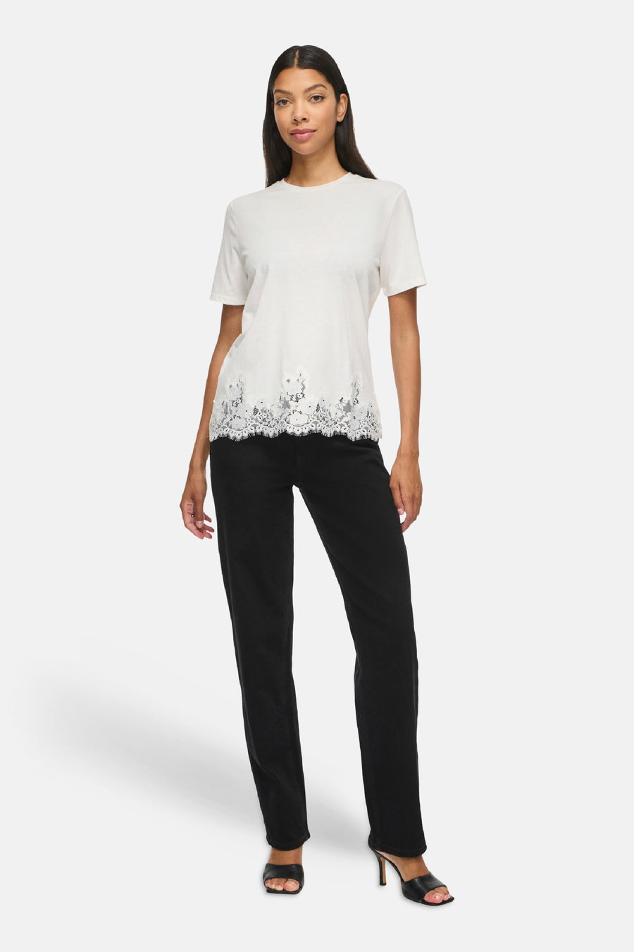 Top blanc uni à manches courtes avec bordure dentelle au bas, par VILA®, porté avec pantalon noir et sandales à talons, vue de face.