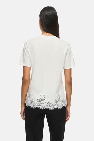 Top blanc à manches courtes avec bordure en dentelle au bas, de VILA®, vue arrière sur modèle portant un pantalon noir