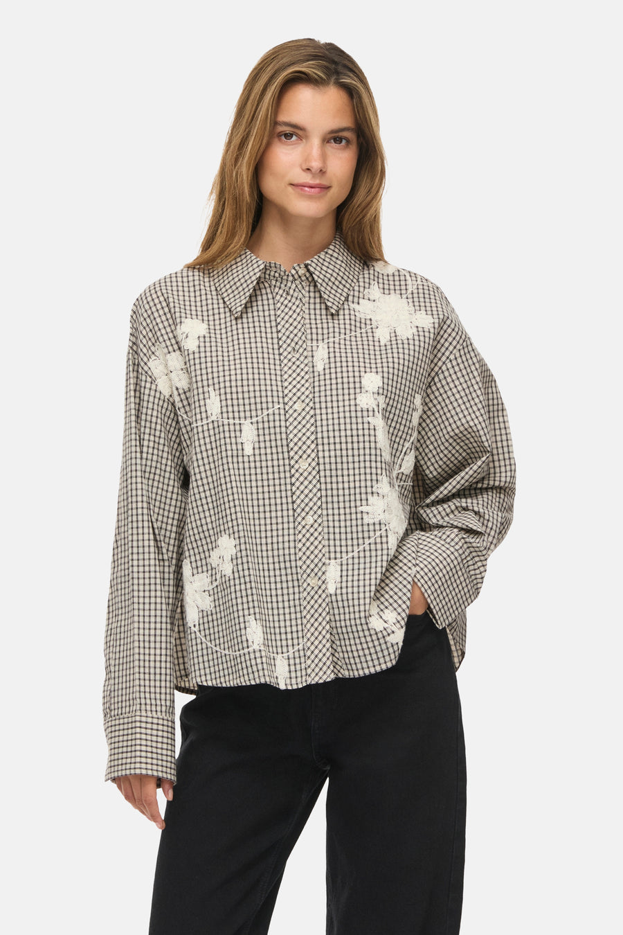Long-sleeve gingham blouse with white floral embroidery, worn by model with black pants, front view